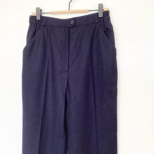 May include: Navy blue high-waisted pants with a button closure and side pockets. The pants are hanging on a wooden hanger. The fabric appears to be a medium-weight material.