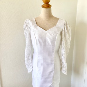 May include: A white dress with a lace bodice and long sleeves. The dress has a fitted silhouette and a V-neckline.