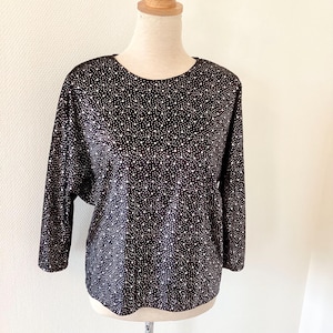 Può includere: Una blusa di velluto nero con un motivo a pois bianchi. La blusa ha una scollatura rotonda e maniche a tre quarti.