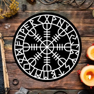 May include: A black and white circular Viking symbol, the Vegvísir, on a wooden surface. The symbol is surrounded by other objects, including candles, a book, and jewelry. The Vegvísir is a symbol of guidance and protection.