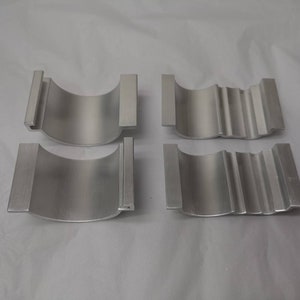 May include: Four silver metal parts, two with a smooth surface and two with a textured surface. The parts are shaped like half-cylinders.