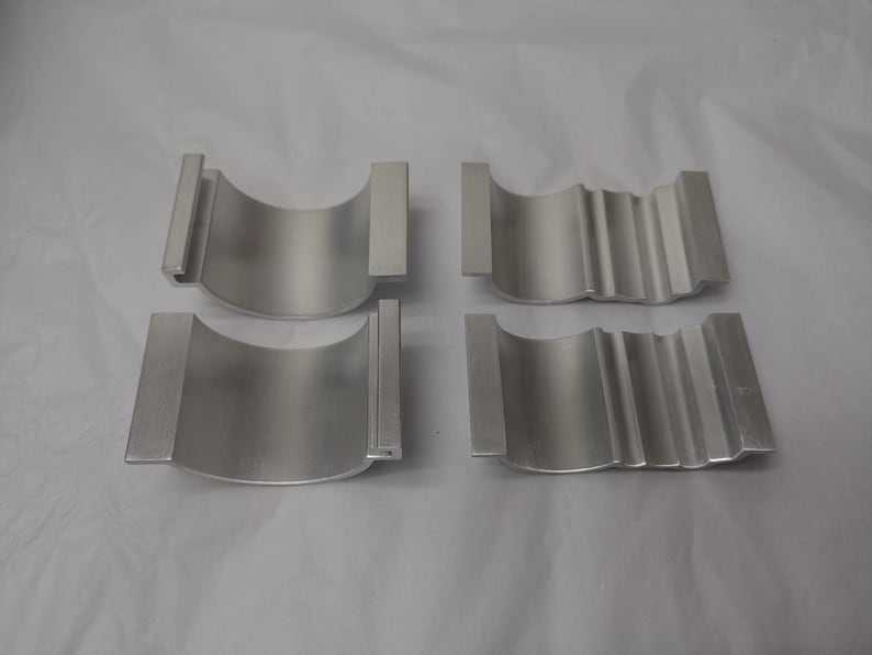 May include: Four silver metal parts, two with a smooth surface and two with a textured surface. The parts are shaped like half-cylinders.