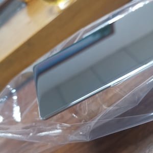 May include: A silver-colored metal rectangle wrapped in clear plastic. The metal has a reflective surface.