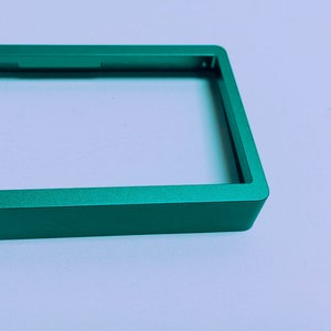Puede incluir: Un marco de metal verde con una abertura rectangular. El marco est&aacute; hecho de metal liso y cepillado.