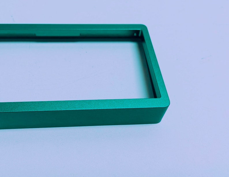 Puede incluir: Un marco de metal verde con una abertura rectangular. El marco est&aacute; hecho de metal liso y cepillado.