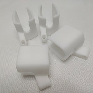Peut inclure: Quatre objets en plastique blanc imprim&eacute;s en 3D. Les objets sont en forme de U avec un petit trou au fond.