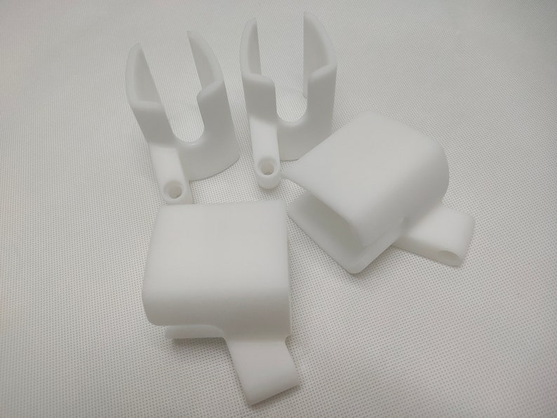 Peut inclure: Quatre objets en plastique blanc imprim&eacute;s en 3D. Les objets sont en forme de U avec un petit trou au fond.
