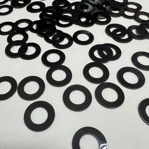 Puede incluir: Un montón grande de arandelas de plástico negro, algunas están dispersas sobre una superficie blanca.