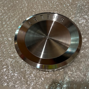 May include: A silver metal disc with the word "SHELBY" engraved around the edge.