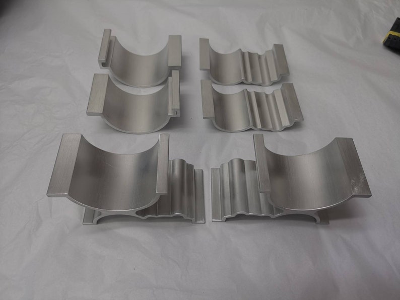 May include: Six silver metal brackets with a curved shape and a ribbed design. The brackets are arranged in two rows of three.