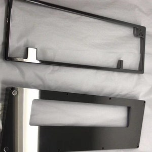 Könnte beinhalten: Zwei schwarze Metallplatten mit Ausschnitten. Die obere Platte ist rechteckig mit einem kleineren rechteckigen Ausschnitt in der Mitte. Die untere Platte ist rechteckig mit einem größeren rechteckigen Ausschnitt in der Mitte. Beide Platten sind glänzend und haben eine glatte Oberfläche.