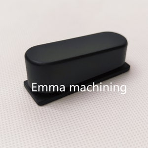 May include: A black plastic stapler with a rectangular base and a rounded top. The stapler has the text "Emma machining" printed on the base.