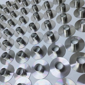 May include: A close-up view of a large quantity of silver metal rings with a raised lip. The rings are arranged in rows on a white surface.