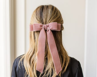 May include: A dusty rose velvet hair bow with long tails tied in a bow at the back of the head.