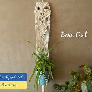 May include: A macrame owl wall hanging with a plant in a blue pot hanging from the bottom. The owl is made of natural colored cord and has wooden eyes. The text "Barn Owl" is written in white on a beige background. The text "Designed and produced by Ukrainians" is written in blue and yellow on a white background.
