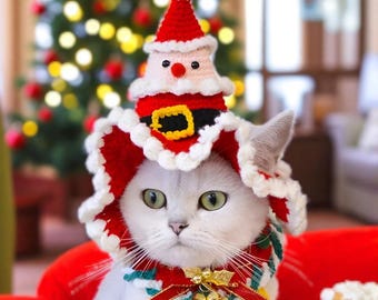 May include: A white cat wearing a red and white crocheted Santa Claus hat and collar. The hat features a Santa face and a black belt with a gold buckle. The cat is sitting in front of a Christmas tree.