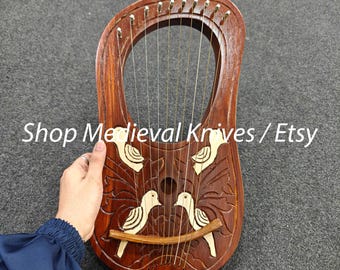 Może przedstawiać: Drewniana lira z rzeźbionymi wzorami ptaków i liści. Instrument posiada struny i zakrzywiony kształt. Tekst "Shop Medieval Knives / Etsy" jest widoczny na zdjęciu.