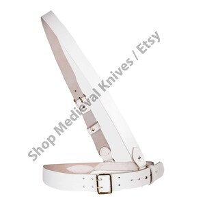 May include: A white leather sword belt with a shoulder strap and a waist belt. The belt has brass buckles and rivets. The text "Shop Medieval Knives / Etsy" is visible.