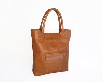 May include: A brown leather tote bag with a single pocket on the front. The bag has two top handles.