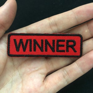 May include: Red fabric patch with black stitching and the word "WINNER" in black lettering.