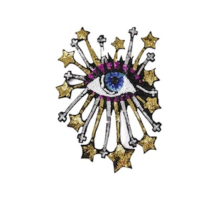 May include: A blue eye with white iris and black pupil surrounded by gold and silver sequins in the shape of stars. The eye is surrounded by a black outline and a pink and purple border.
