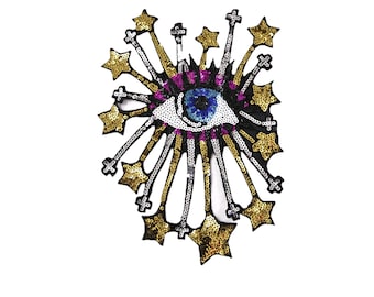 Könnte beinhalten: Ein blaues Auge mit weißer Iris und schwarzer Pupille, umgeben von goldenen und silbernen Pailletten in Form von Sternen. Das Auge ist von einem schwarzen Umriss und einem rosa-violetten Rand umgeben.