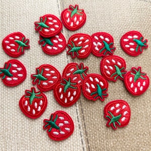 Puede incluir: Una colección de 15 parches bordados de fresa rojos y verdes. Las fresas tienen semillas blancas y hojas verdes.