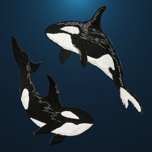 Könnte beinhalten: Zwei gestickte Orca-Wal-Patches in Schwarz und Weiß auf dunkelblauem Hintergrund.