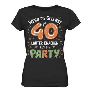 Könnte beinhalten: Schwarzes T-Shirt mit dem Text "Wenn die Gelenke 40 lauter knacken als die Party" in Weiß, Orange und Grün. Die Zahl 40 ist orange mit einem Stern in der Mitte. Das Shirt hat einen Rundhalsausschnitt.