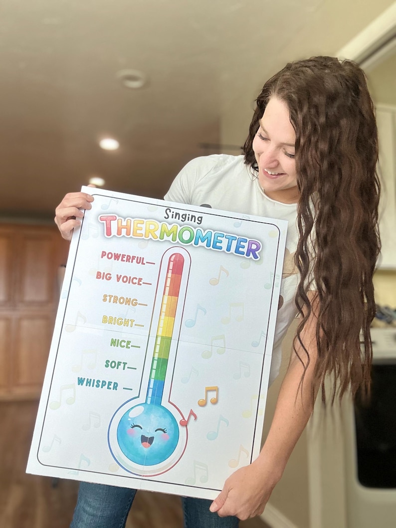 May include: A colorful "Singing Thermometer" poster with a cartoon thermometer design. The thermometer scale ranges from "Whisper" to "Powerful," with musical notes and a smiling face. The poster is held by a person.