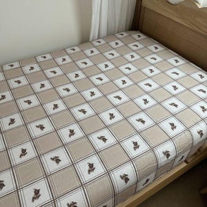 May include: A beige fitted sheet with a brown and white plaid pattern and a repeating design of brown rabbits. The sheet is on a wooden bed frame.