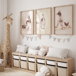 Puede incluir: Una estanter&iacute;a de madera clara con cubos de almacenamiento blancos, un banco de madera clara con tres almohadas y tres ilustraciones enmarcadas de una ni&ntilde;a, un ganso y una ni&ntilde;a con pollos. Las ilustraciones est&aacute;n en un marco marr&oacute;n claro con un paspart&uacute; blanco.