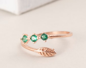 May include: A rose gold ring with a leaf design and four green gemstones.