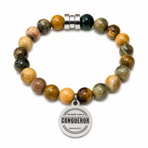 Könnte beinhalten: Ein Perlenarmband mit runden, polierten Steinen in Braun-, Beige- und Dunkelgrüntönen. Das Armband enthält drei silberfarbene Metallabstandshalter und einen runden, silberfarbenen Anhänger mit der Gravur I AM MORE THAN A CONQUEROR Romans 8:37.