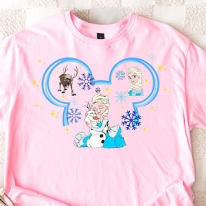 A pink t-shirt with a cartoon design featuring characters from the Disney movie Frozen, including Elsa, Olaf, and other beloved characters.
