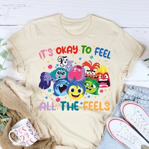 May include: A beige t-shirt with the text "It's okay to feel all the feels" and a graphic of the characters from the movie Inside Out.