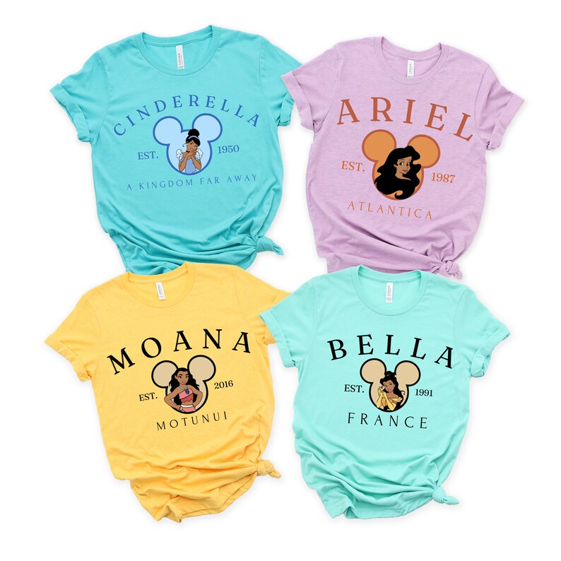 以下が含まれることがあります： ディズニーのプリンセスをデザインしたTシャツが4枚。それぞれのTシャツには、プリンセスの画像、プリンセスの名前、映画の公開年が描かれています。Tシャツの色は、青、紫、黄、緑です。