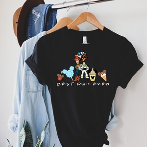 May include: Black t-shirt with a graphic of Woody and Buzz Lightyear from Toy Story, Mickey Mouse, and other Disney characters. The text "BEST DAY EVER" is printed below the graphic.
