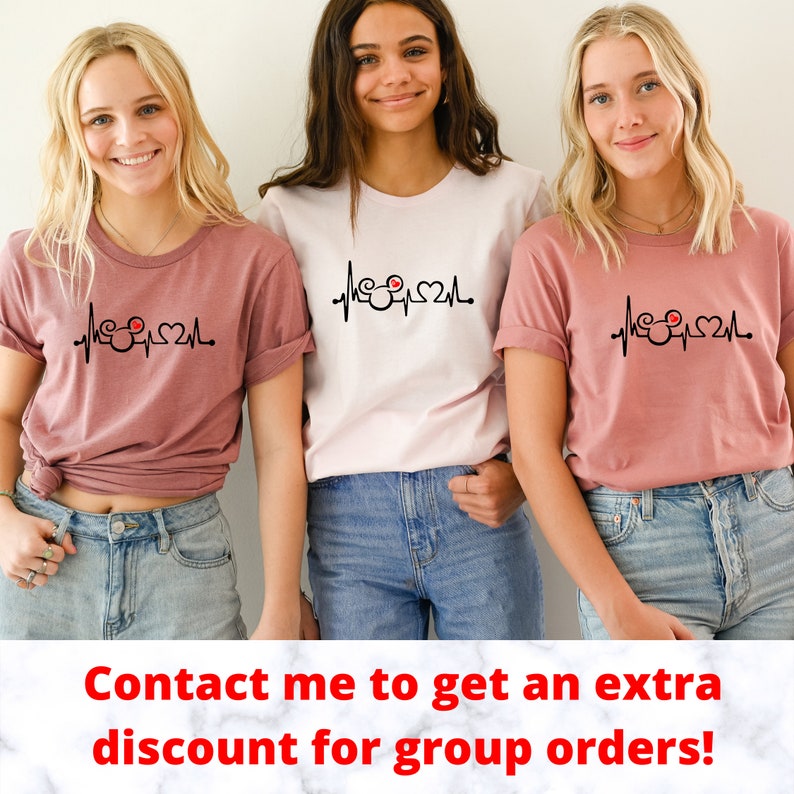 May include: Three women wearing pink and white t-shirts with a black and red Mickey Mouse heartbeat graphic. The text "Contact me to get an extra discount for group orders!" is at the bottom of the image.