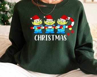 May include: Green Christmas sweater with three green aliens wearing Santa hats holding a candy cane with the text "CHRISTMAS" underneath.