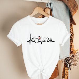 May include: White t-shirt with a black and red graphic of a heartbeat with Mickey Mouse ears and a heart.