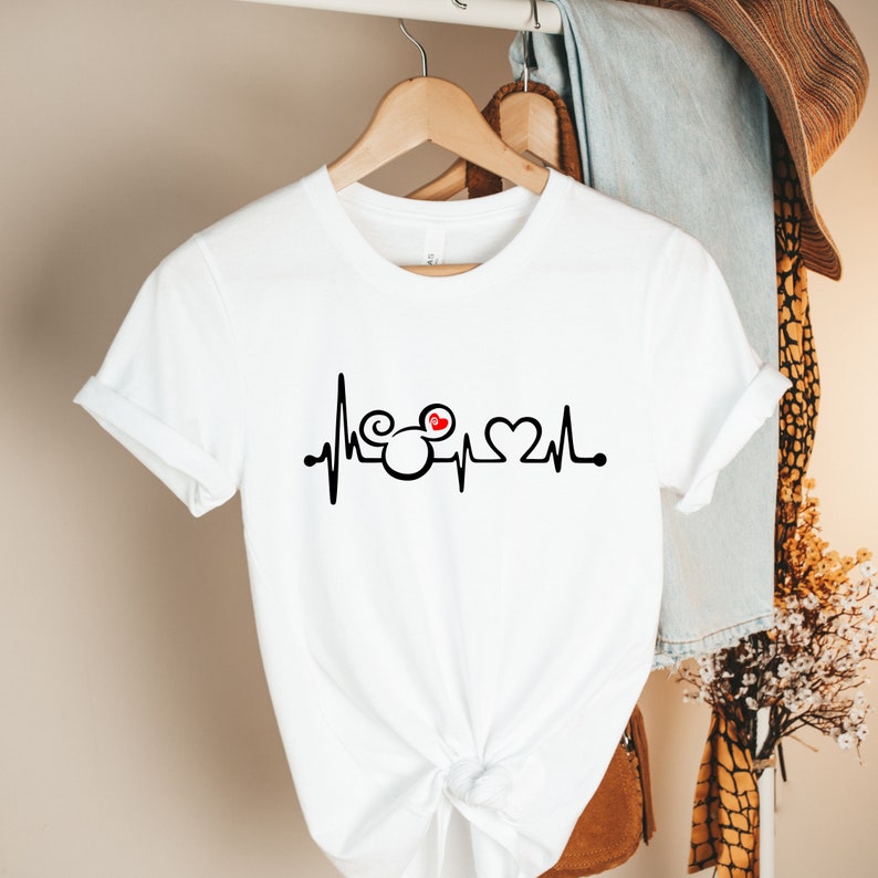 May include: White t-shirt with a black and red graphic of a heartbeat with Mickey Mouse ears and a heart.