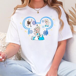 A woman wearing a white t-shirt with a Disney character design, including Elsa, Olaf, and other characters from the Disney movie Frozen.