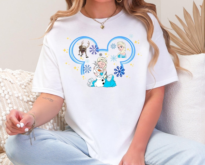 A woman wearing a white t-shirt with a Disney character design, including Elsa, Olaf, and other characters from the Disney movie Frozen.