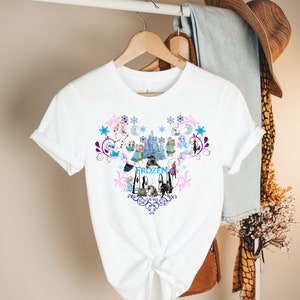 Puede incluir: Camiseta blanca con un dise&ntilde;o Frozen colorido que presenta personajes como Elsa, Anna, Olaf y Kristoff. El dise&ntilde;o incluye un castillo, copos de nieve y la palabra "Frozen".