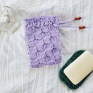 May include: A lavender knitted soap sack with wooden toggles and a bar of soap in a green mesh soap dish.