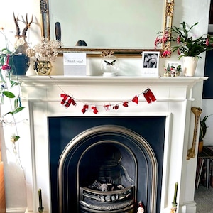 May include: A white fireplace mantel adorned with a gold-framed mirror and festive decorations. A Christmas-themed garland hangs across the mantel. A sign reads "thank you!". The fireplace has a black interior and a metal grate.