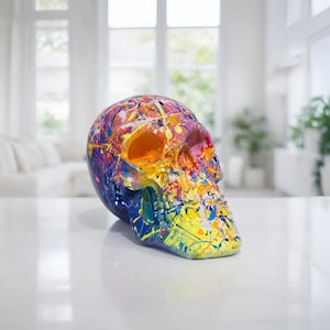 以下が含まれることがあります： 鮮やかなスプラッターペイントデザインのカラフルな装飾スカル彫刻。 スカルは青、黄、オレンジ、ピンクの色合いが混ざり合い、ユニークで芸術的な美しさを生み出しています。 家の装飾に適しています。