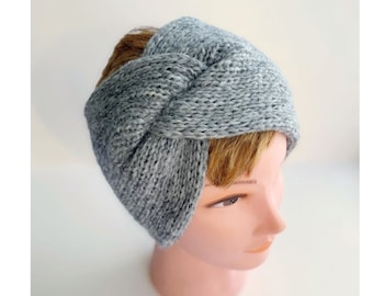 May include: A grey knitted headband with a twisted knot design. The headband is made of a soft, textured yarn and is displayed on a mannequin head. The colour is a heathered grey, suitable for various outfits.