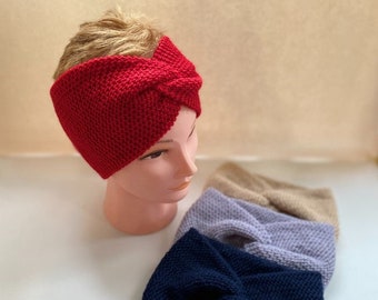 May include: Four knitted headbands in different colours: red, beige, lavender, and navy blue. The headbands are folded in a twisted knot style.
